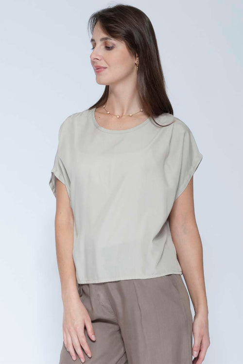 Woman wearing a beige top and brown pants against a white background