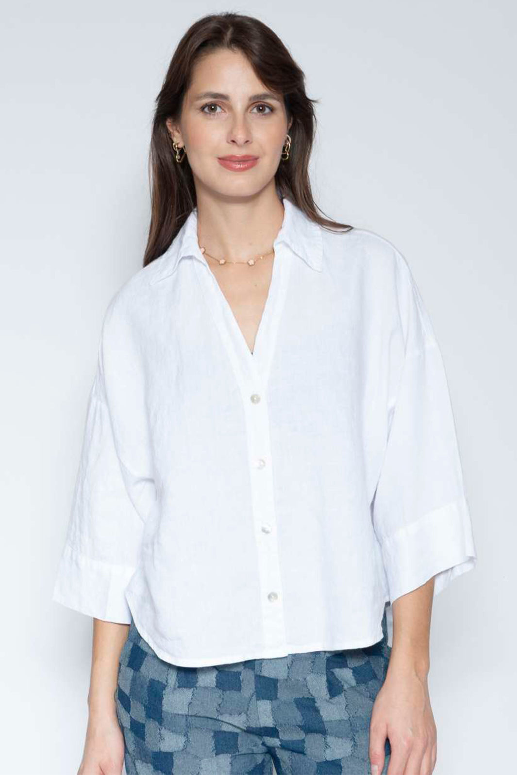 Woman wearing a white shirt and patterned pants against a plain background