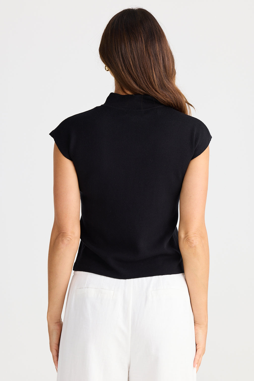 Woman wearing a black sleeveless top and white pants on a light gray background