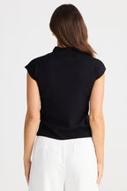 Woman wearing a black sleeveless top and white pants on a light gray background