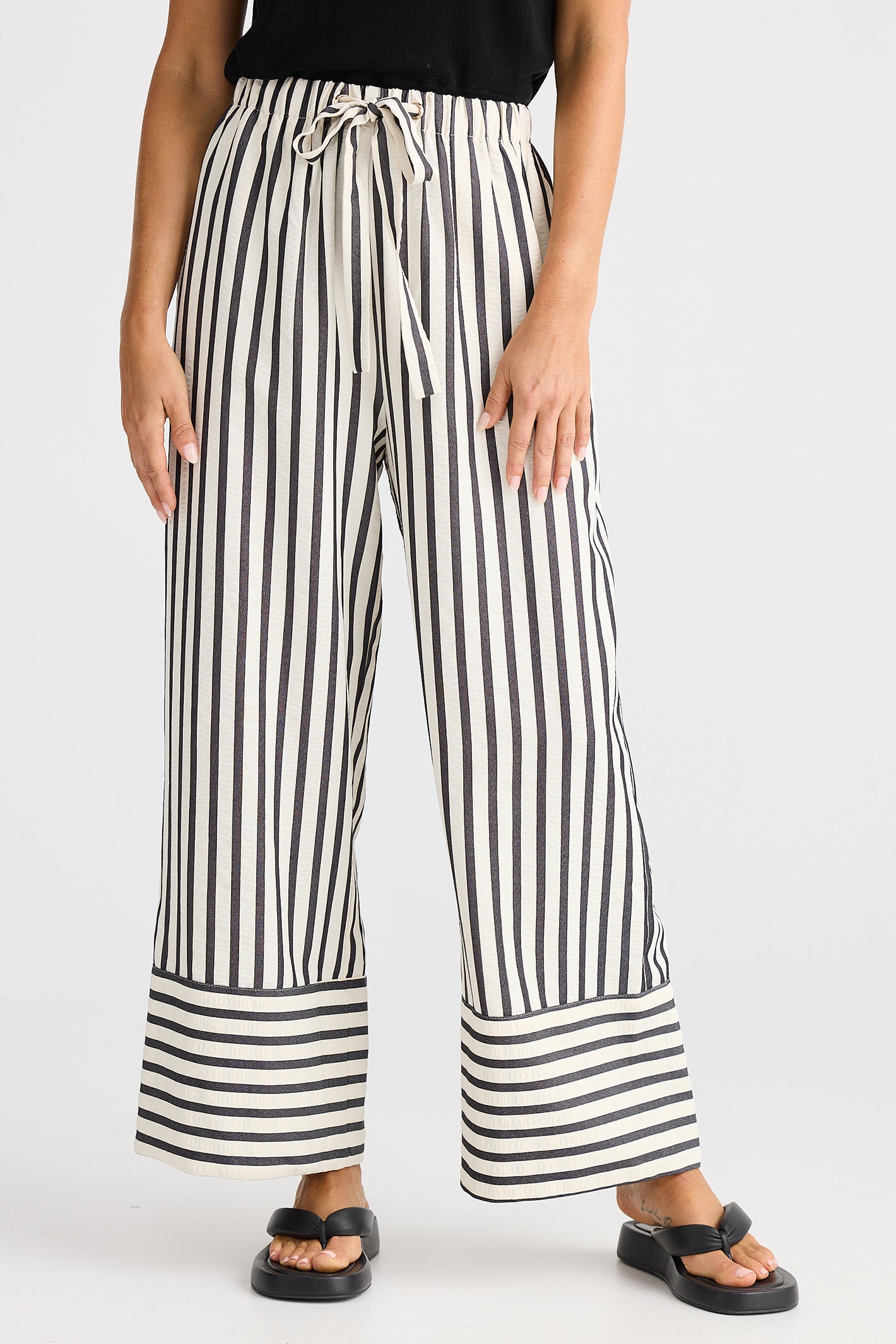 Person wearing black and white striped wide-leg pants on a plain background