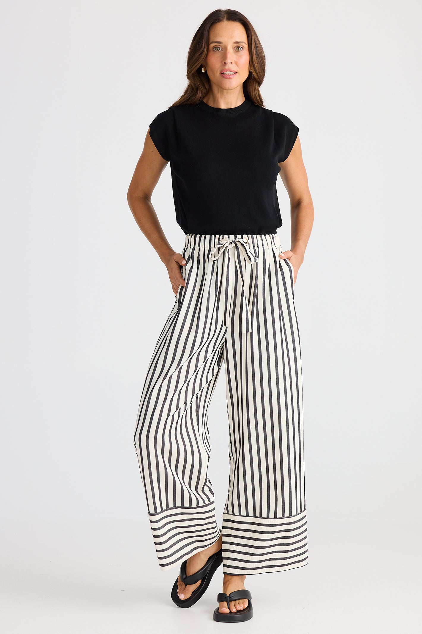 Woman wearing a black top and black and white striped pants on a white background