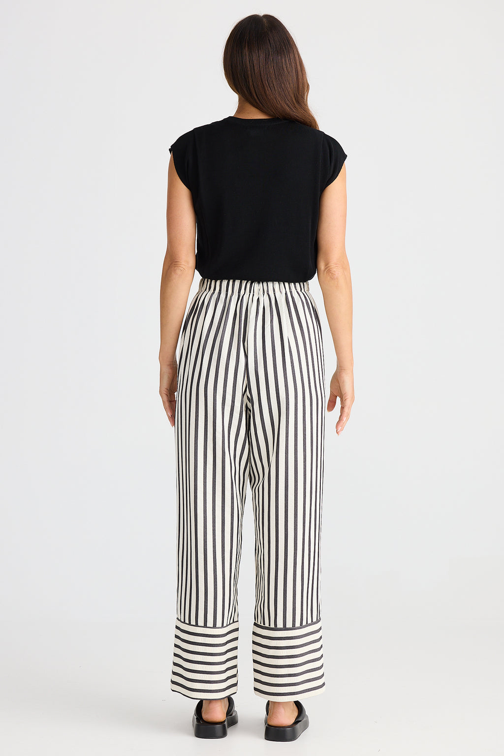 Woman wearing a black top and black and white striped pants on a white background