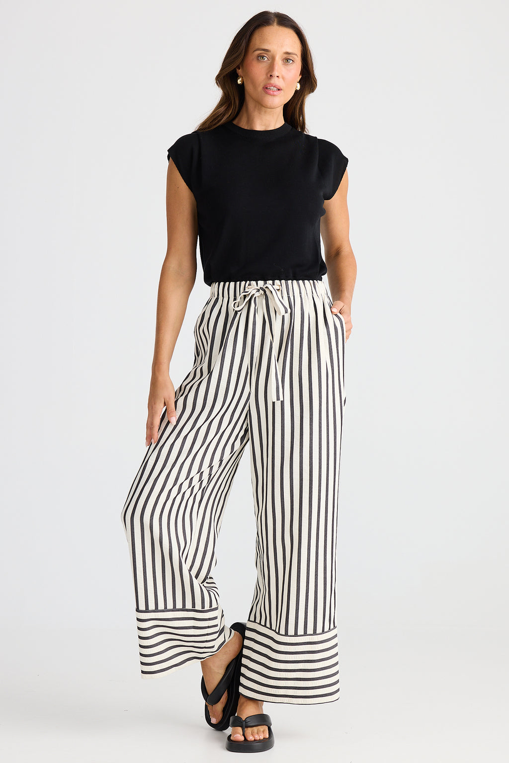 Woman wearing a black sleeveless top and wide-leg striped pants on a white background