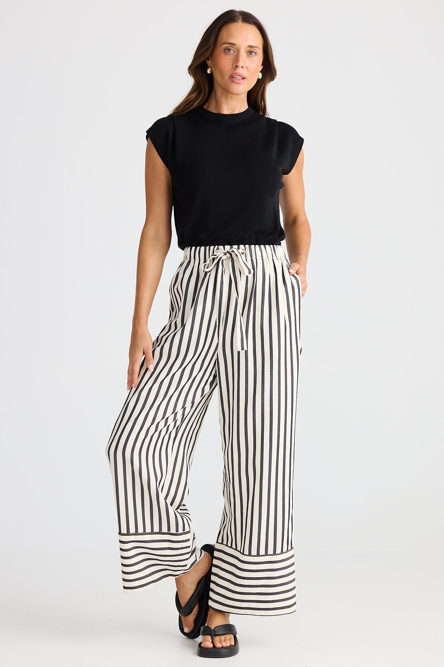 Woman wearing a black sleeveless top and wide-leg striped pants on a white background