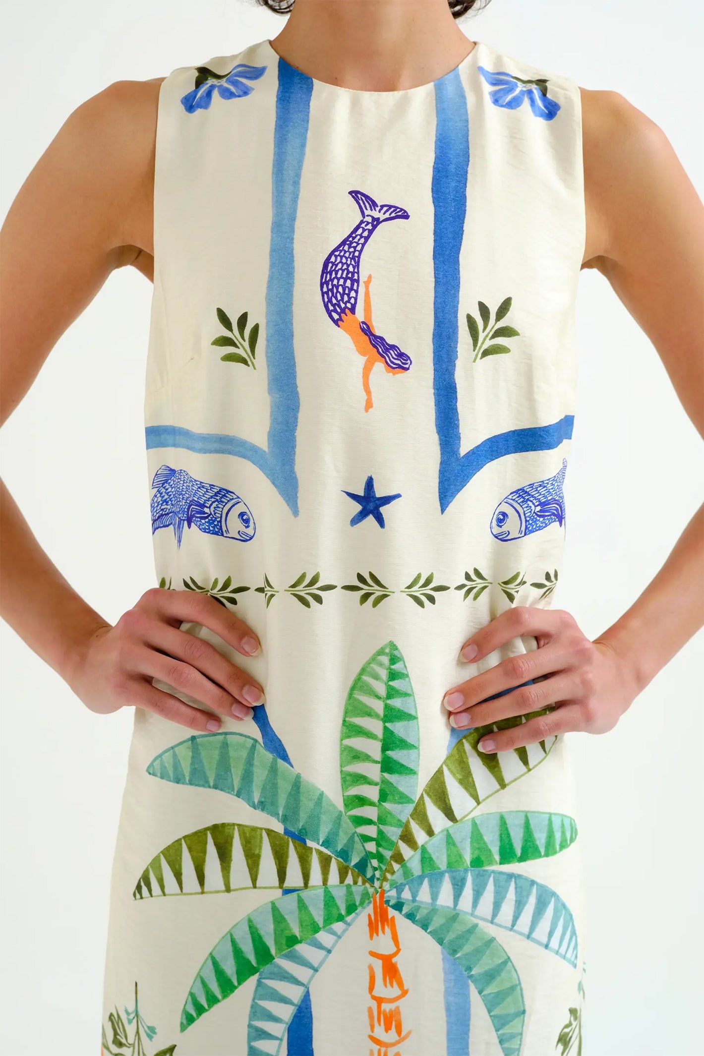 Person wearing a sleeveless dress with colorful animal and plant patterns on a white background