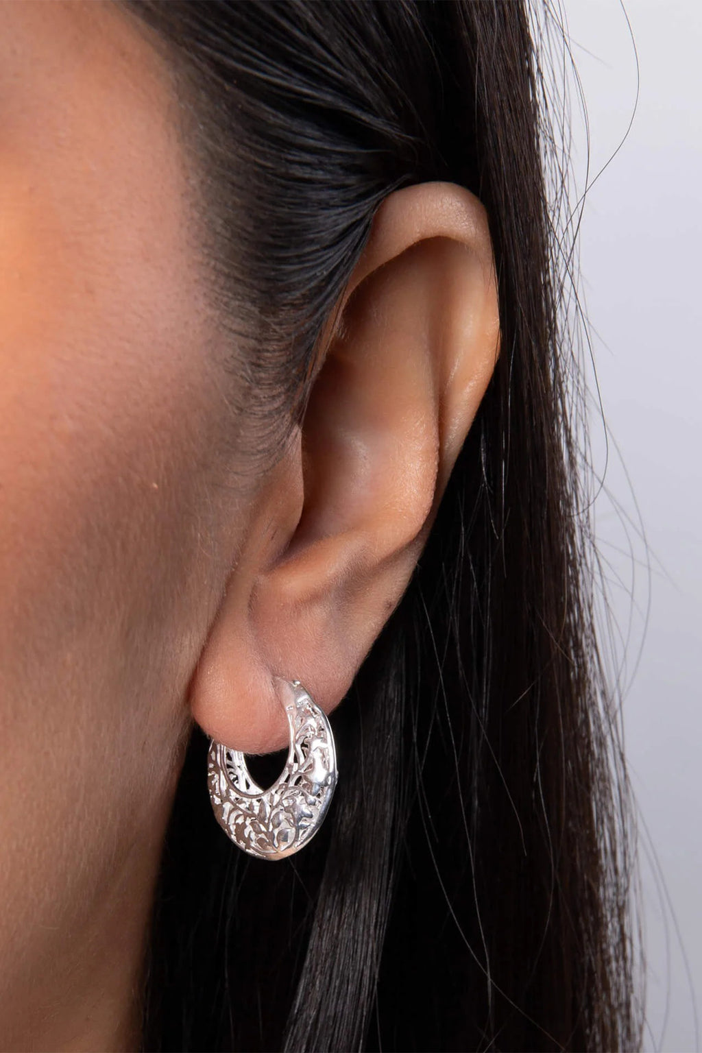 Close-up of an ear wearing a silver hoop earring with a plain background