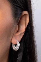 Close-up of an ear wearing a silver hoop earring with a plain background