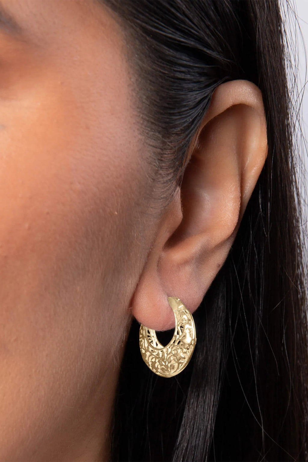 Gold hoop earring worn by a person with dark hair.