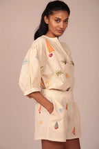 Woman wearing a beige outfit with colorful patterns on a plain background