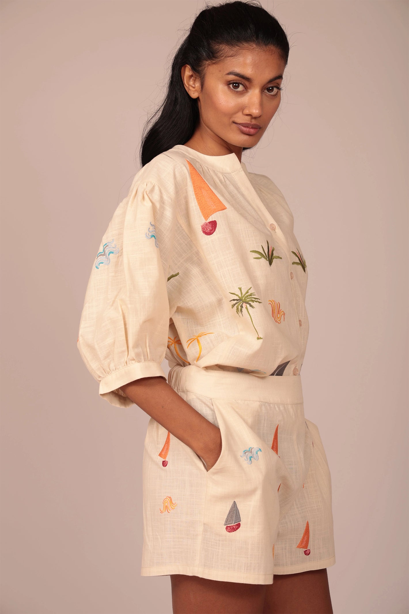 Woman wearing a beige outfit with colorful patterns on a plain background