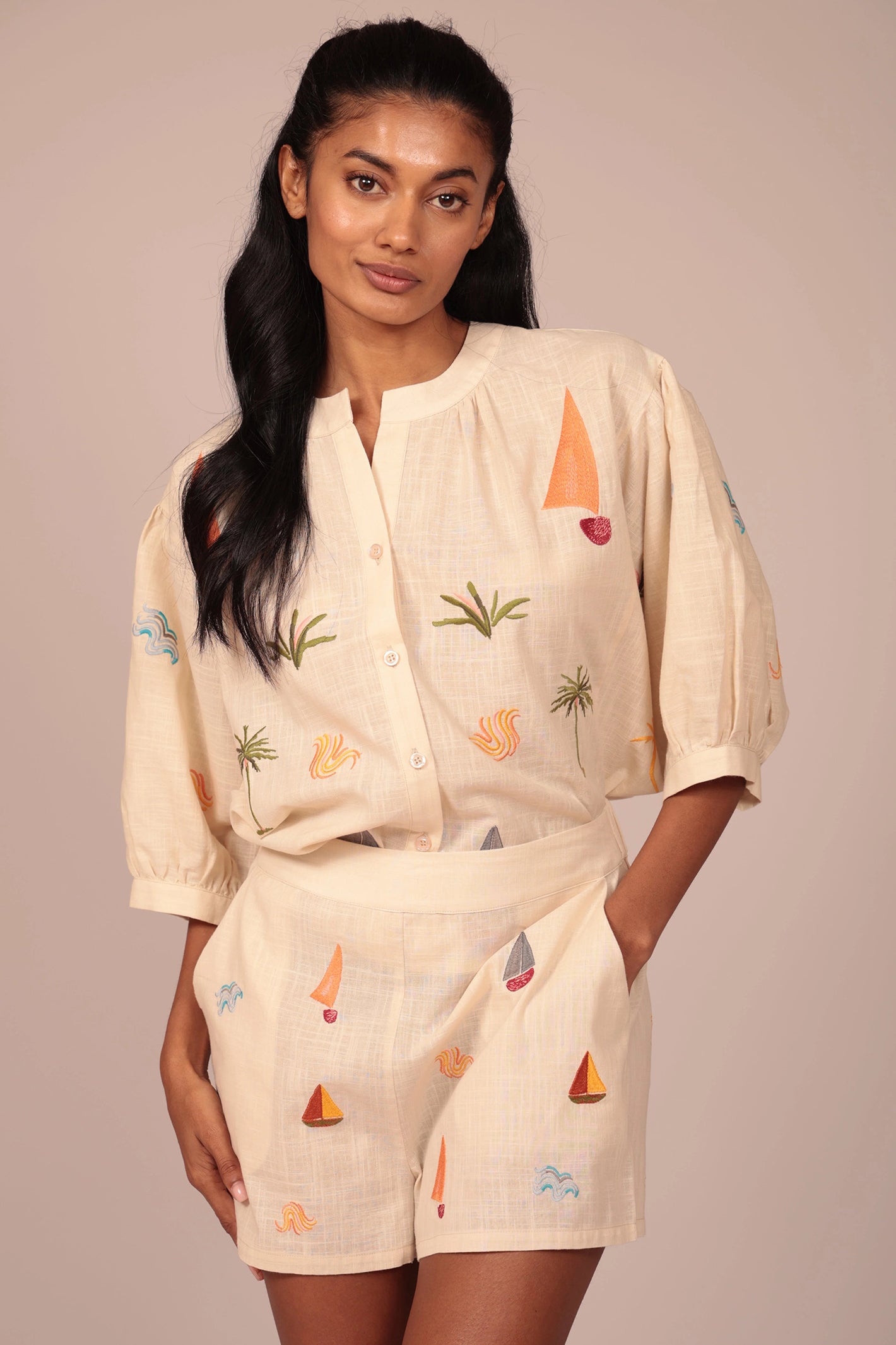 Woman wearing a beige outfit with colorful embroidery on a plain background