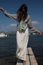 Woman standing on a dock by a body of water wearing a patterned top and white pants.