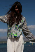 Person wearing a patterned jacket with a colorful pom-pom against a blue sky and water background