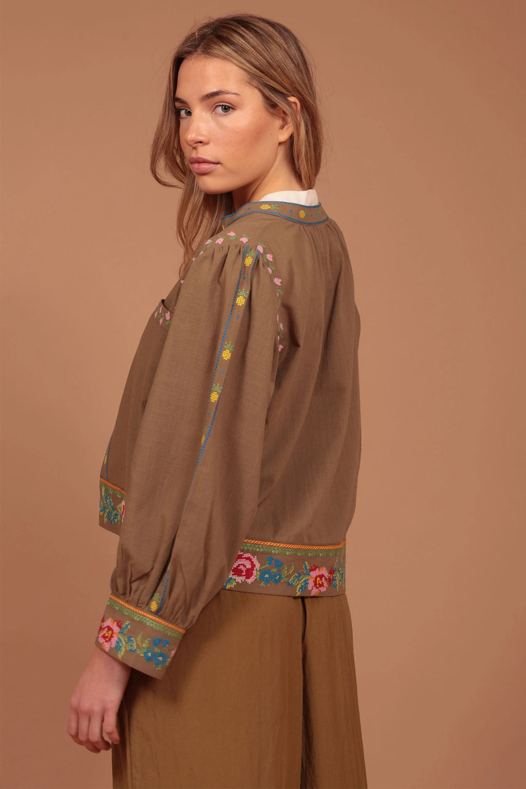 Woman wearing a brown blouse with colorful embroidery on a brown background