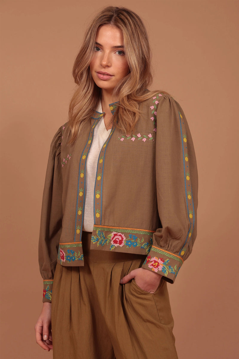 Woman wearing a brown embroidered jacket and pants on a beige background