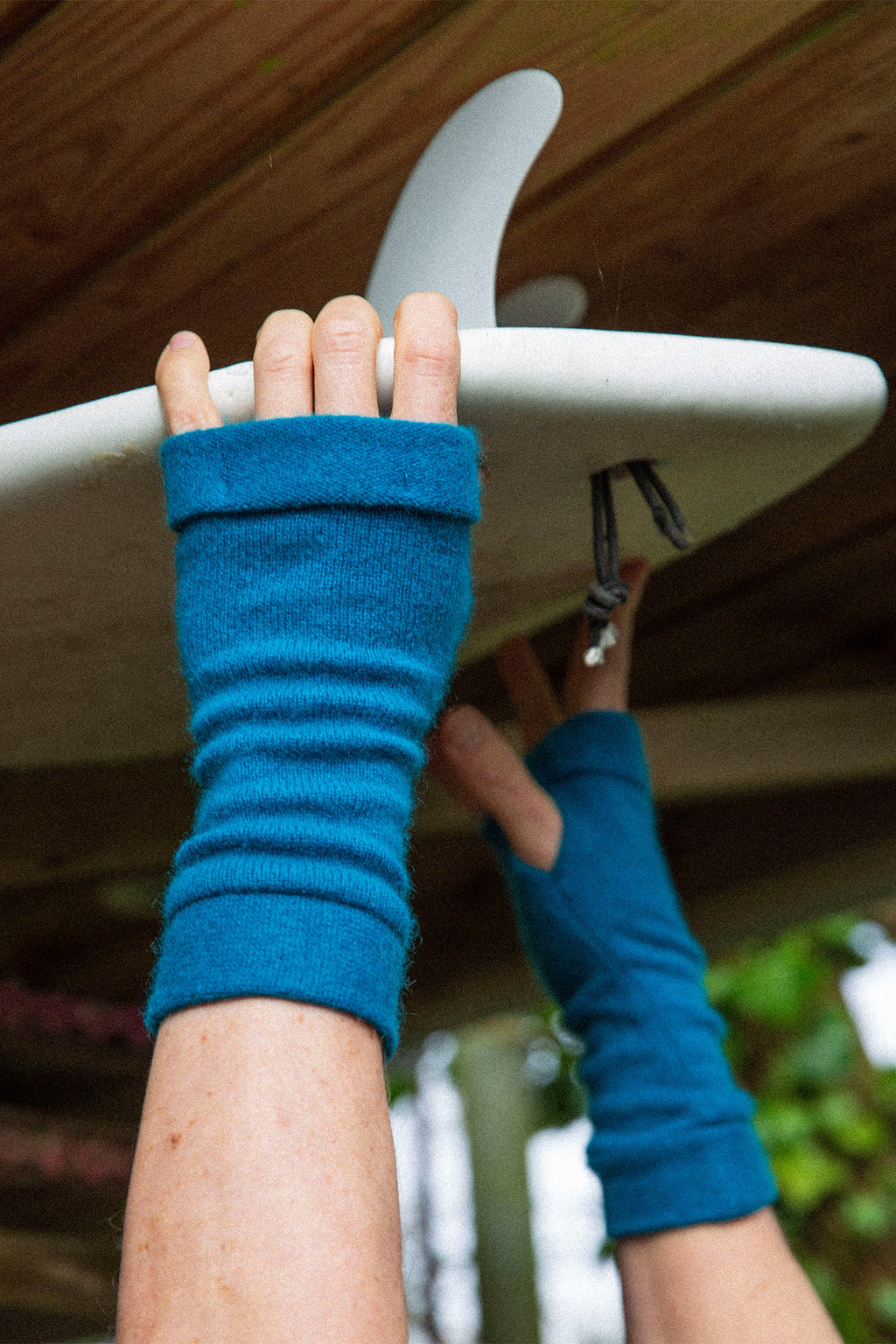 Turtle Doves Teal Blue Cashmere Fingerless Gloves, worn holding a surfboard